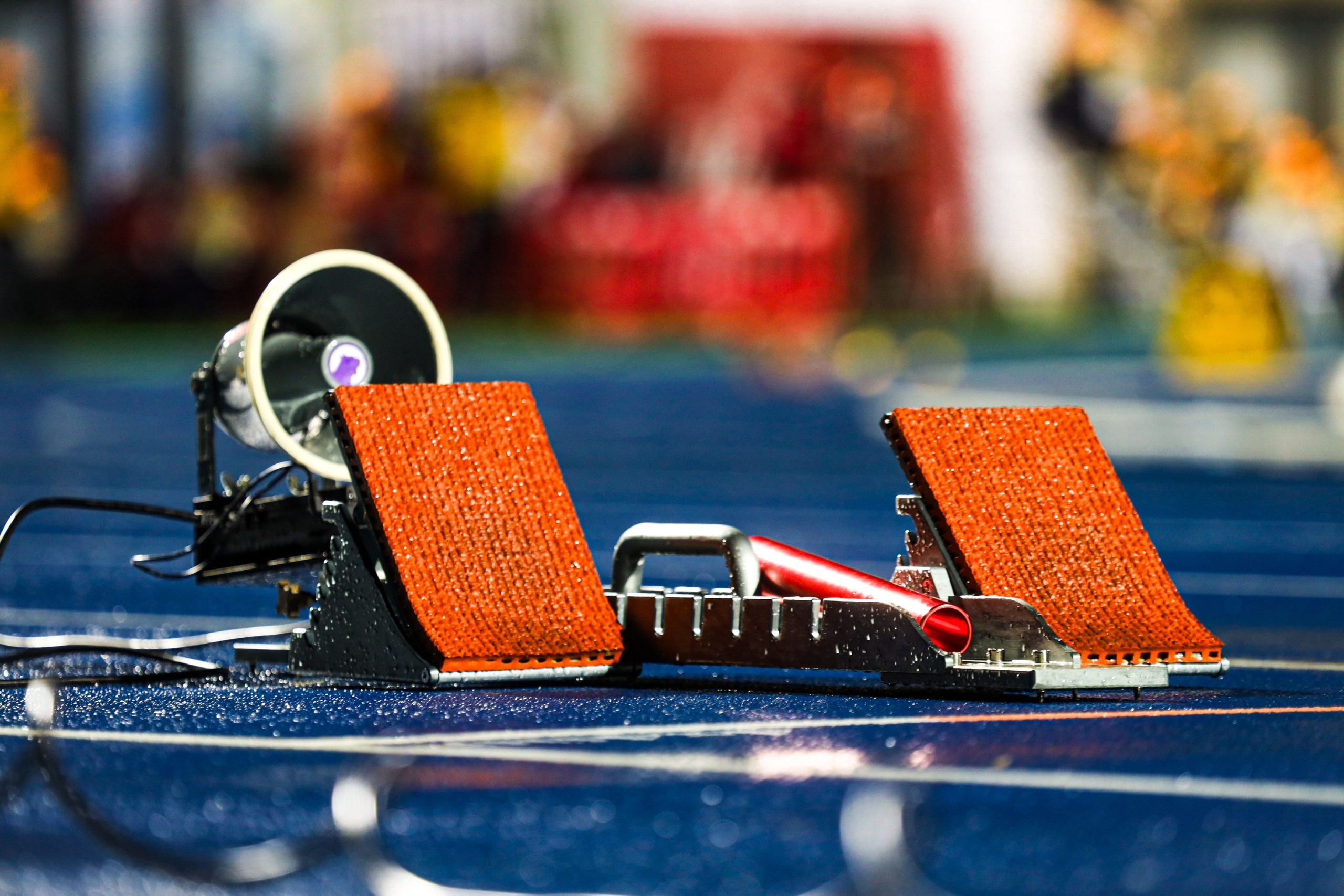 Close-up of athletics starting blocks on a wet blue track, evoking the preparation and precision behind Olympic competition.