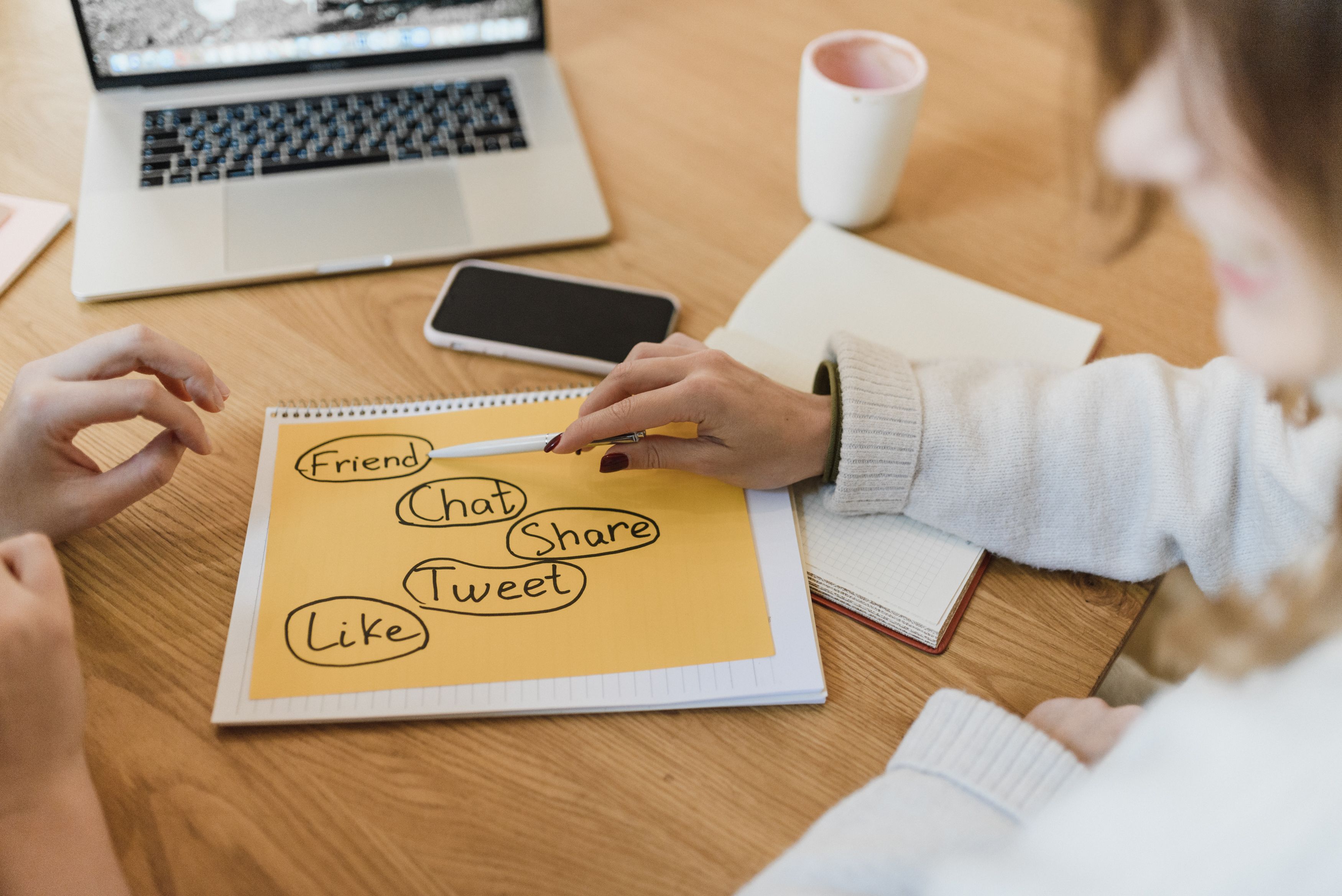 Two women planning a social media marketing strategy with a laptop and smartphone, representing cross-platform editorial planning.